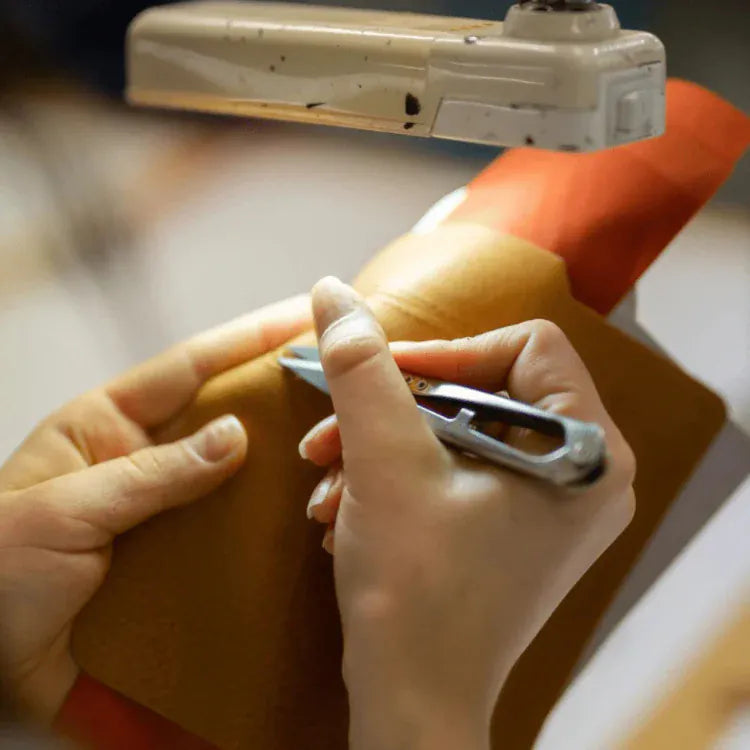 Person using a tool on a leather item with a sewing machine in the background