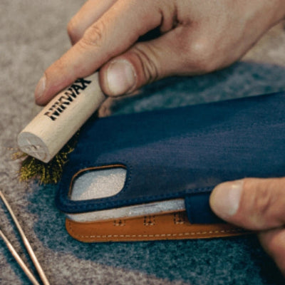 Person using a brush labeled 'Niwax' on a blue leather product.